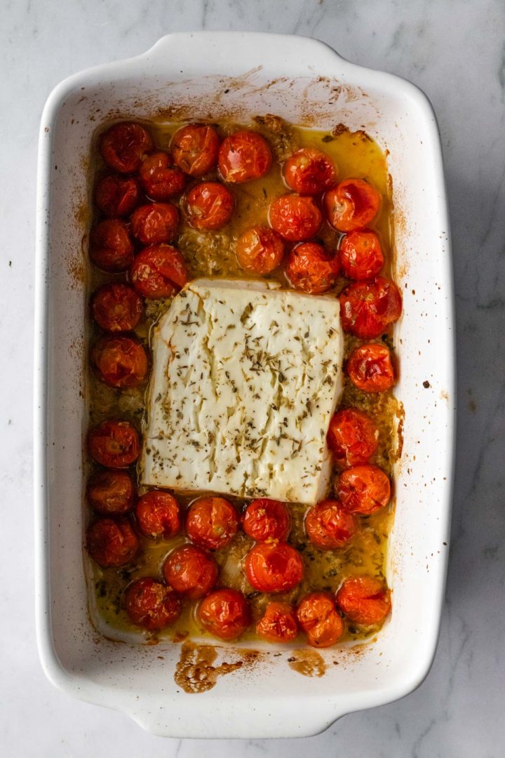 a baking dish with roasted tomatoes, feta cheese and seasoning