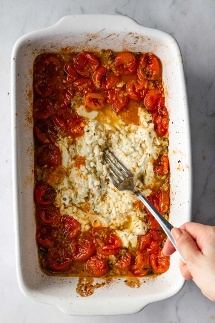 a hand mixing with a fork the mixture of ingredients that is inside of the baking dish