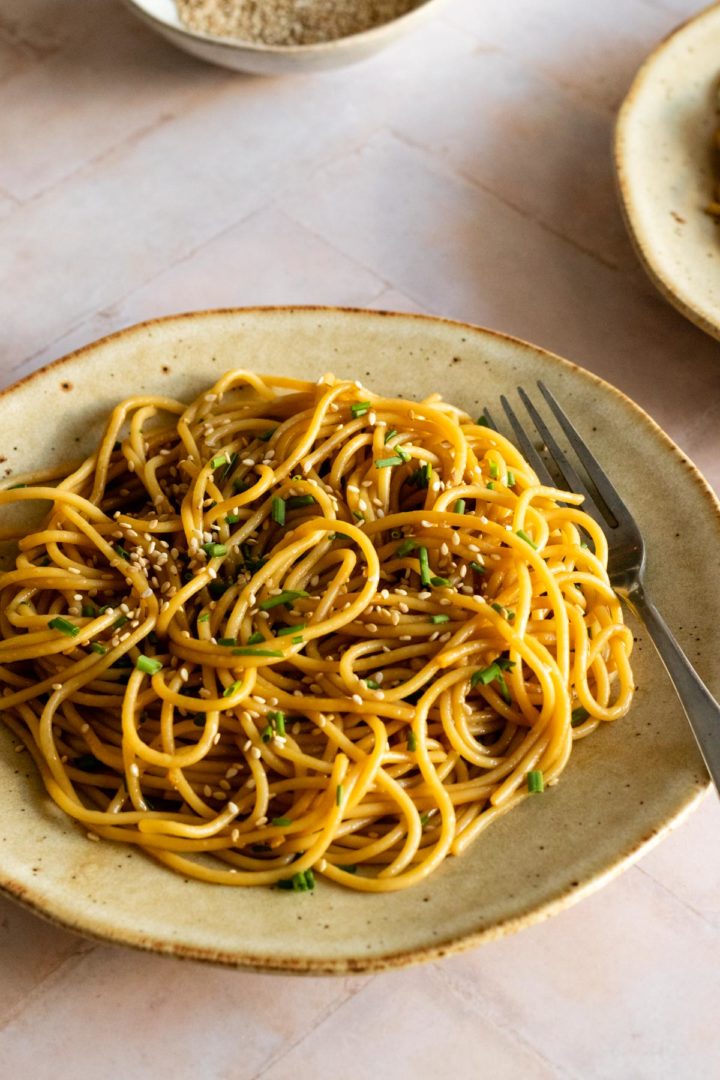a plate served with sesame noodles with sesame seeds and chopped chives on top