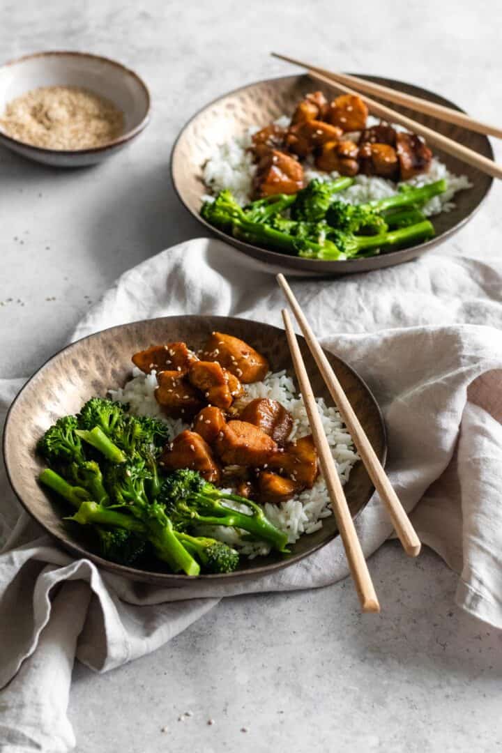 two bowls served with basmati rice, broccolini, chicken and sesame seeds. A small bowl with sesame seeds on the side