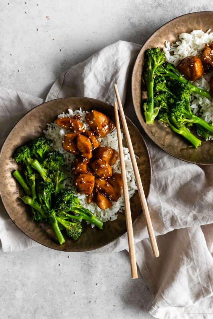 two bowls served with white rice, broccolini, chicken and sesame seeds