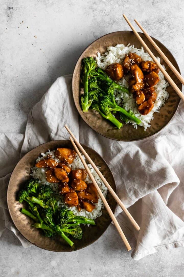 two bowls served with white rice, broccolini, chicken and sesame seeds