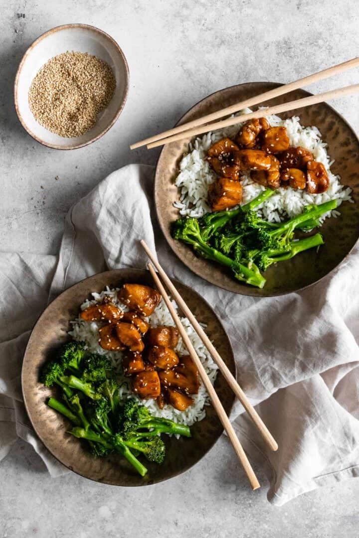 two bowls served with basmati rice, broccolini, chicken and sesame seeds. A small bowl with sesame seeds on the side