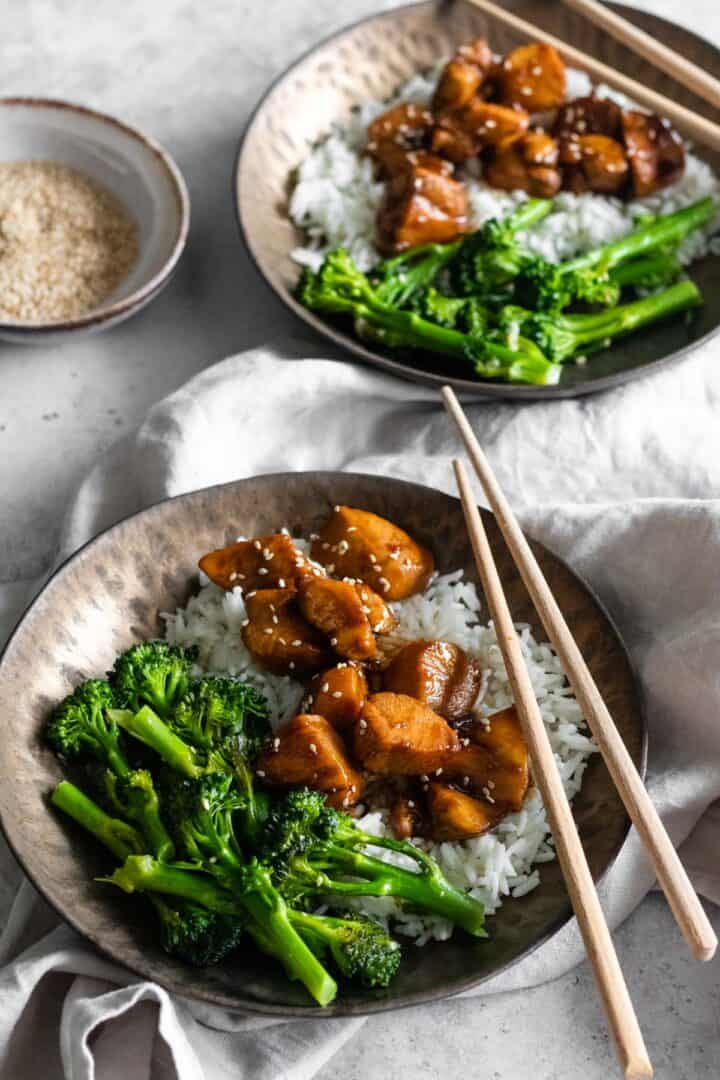 two bowls served with basmati rice, broccolini, chicken and sesame seeds. A small bowl with sesame seeds on the side