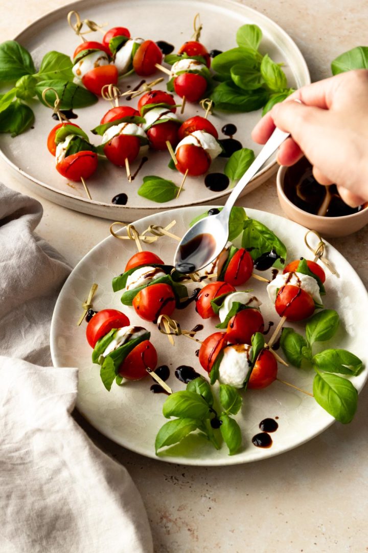 a hand holding a spoon with balsamic glaze over the skewers