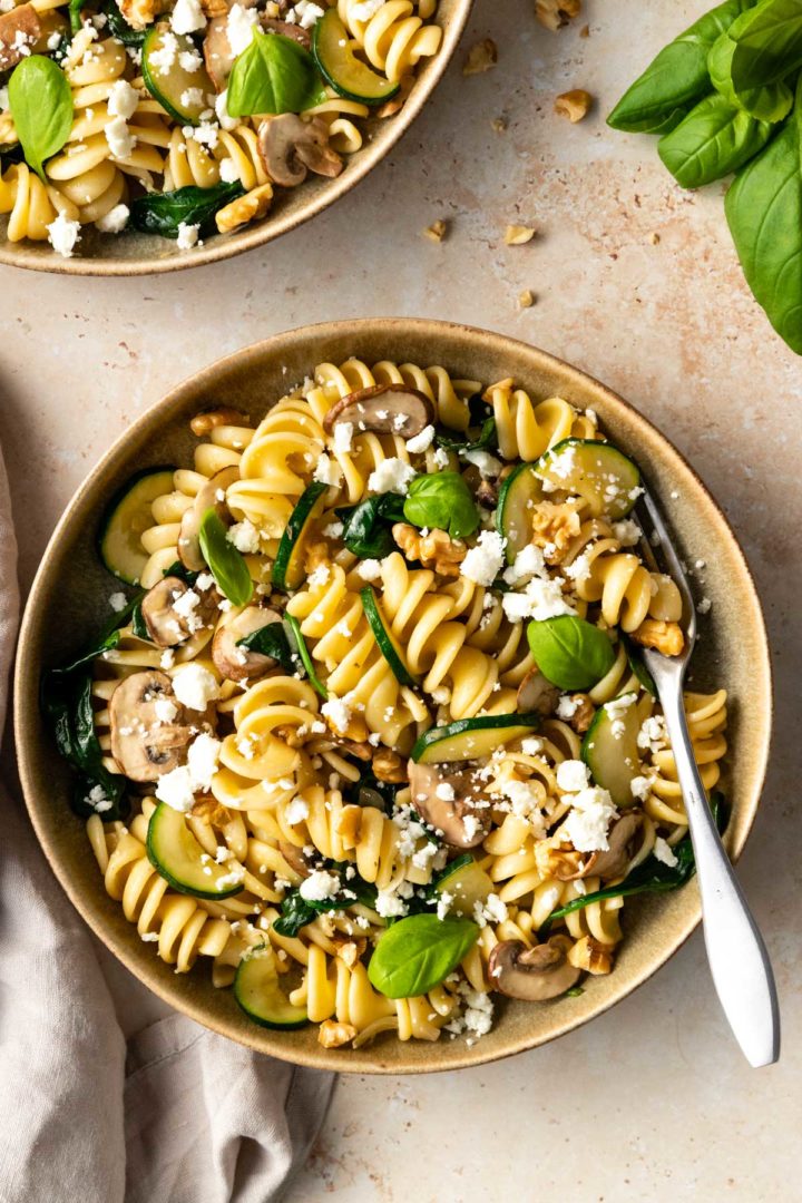 one plate served with pasta, zucchini, mushrooms, spinach, crumbled feta and walnuts.