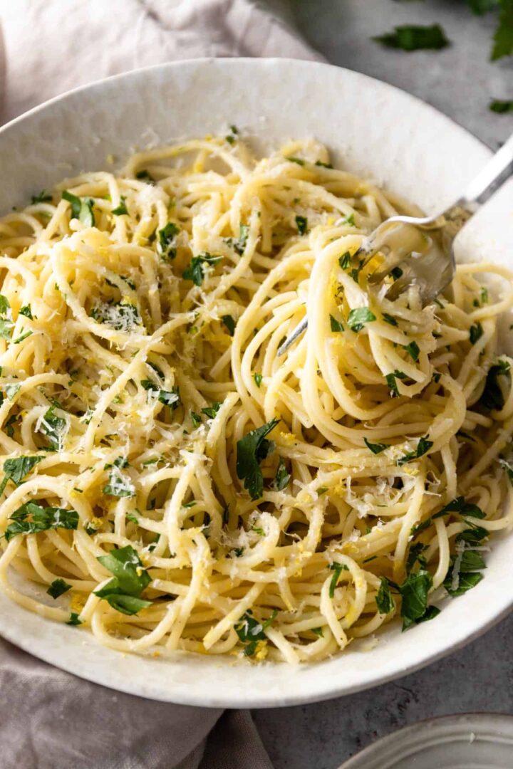 a bowl with spaghetti pasta with lemon zest, parmesan and chopped parsley