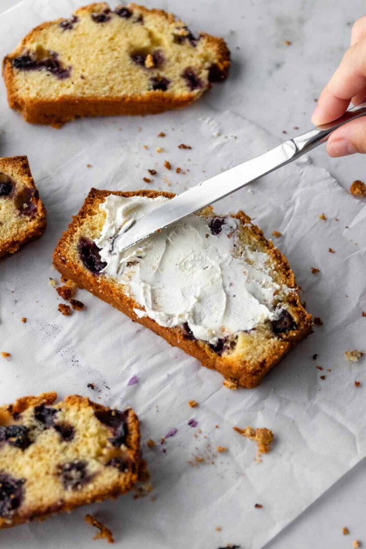 slices of lemon blueberry loaf on top of parchment paper and one of them with cream cheese on top
