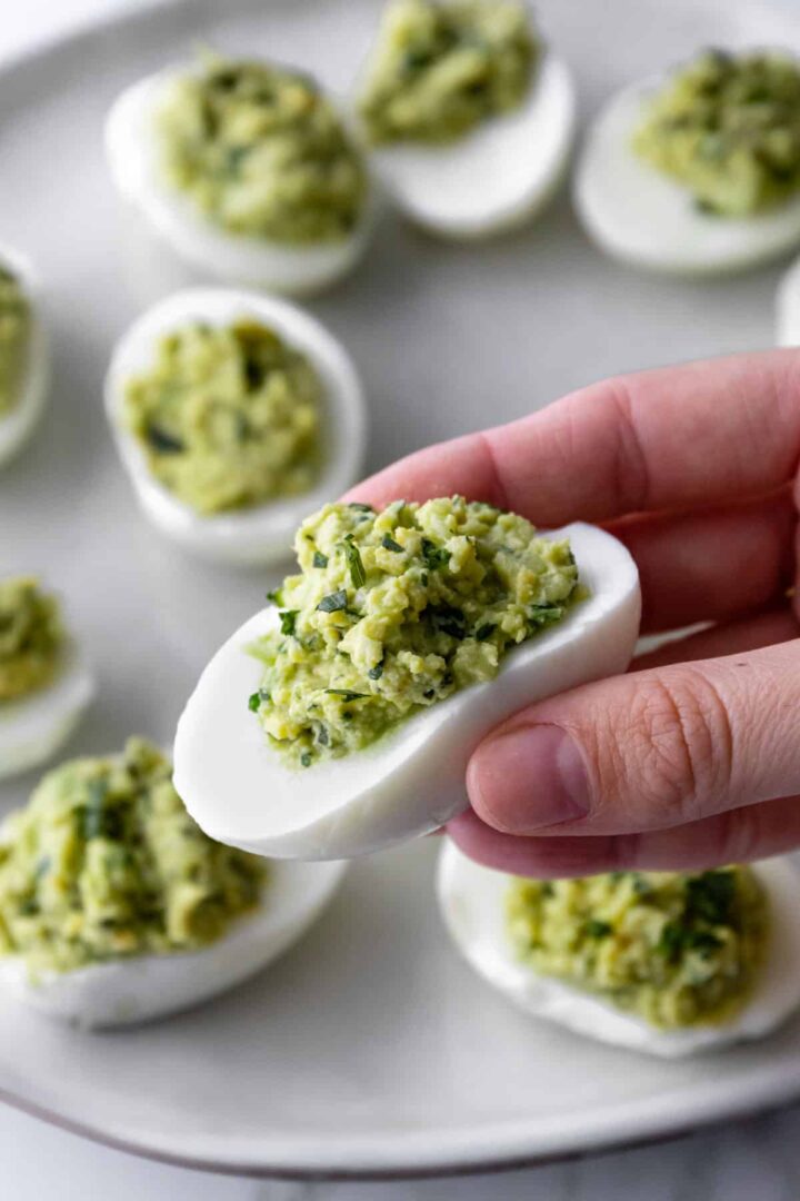 a hand holding a boiled egg with avocado filling inside