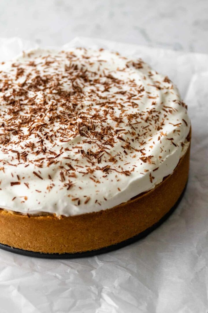 a banoffee pie with whipped cream and chocolate shaving on top of parchment paper