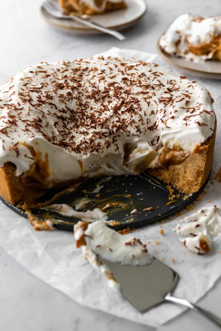 a banoffee pie garnished with chocolate shavings on top of parchment paper and a marble board