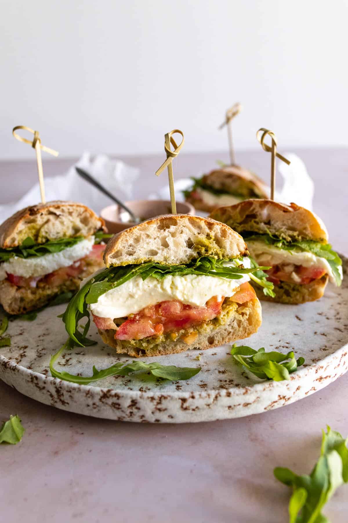 a plate with four sandwiches with arugula, mozzarella, tomato, and pesto