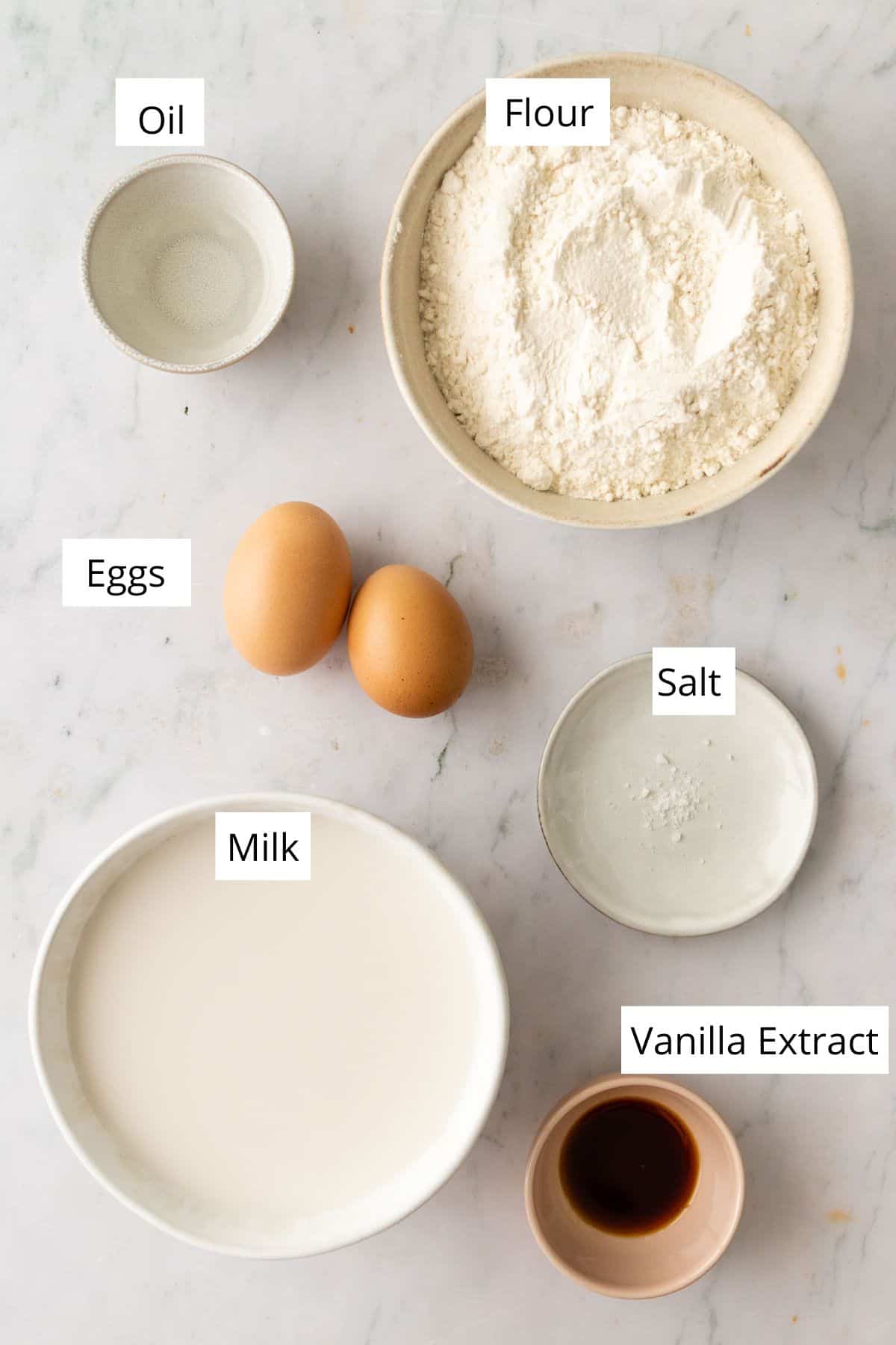 ingredients to make crepes inside of bowls. Two eggs on top of a marble board